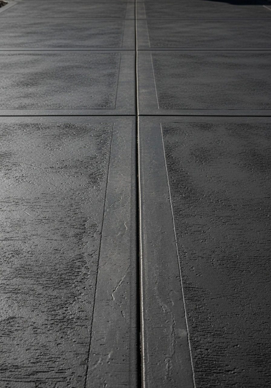 Charcoal broom-finish concrete driveway with integral dark pigment and clean brushed texture, residential front approach in afternoon light