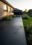 Charcoal poured concrete backyard patio extending from a dark grey fibre cement bungalow, golden hour light