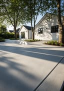 Light grey raw poured concrete backyard patio, white rendered bungalow, dappled tree-canopy shade
