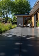 Charcoal raw poured concrete patio, flat-roof concrete-and-timber home, lounge chairs, afternoon sun