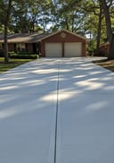 Light grey raw poured concrete double driveway, ranch-style home, dappled morning shade