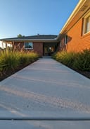 Light grey raw poured concrete side-entry path, ranch-style home, native grasses, golden hour