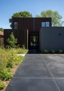 Near-black polished poured concrete side path, Corten steel home, 3/4 angle, midday sun