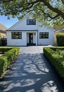 Near-black raw poured concrete side-entry path, white rendered bungalow, box hedges, afternoon light