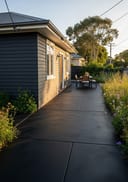 Near-black raw poured concrete courtyard patio, dark timber board-clad home, golden hour 3/4 angle