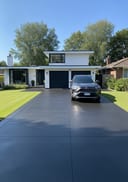 Near-black polished poured concrete driveway, cantilevered bungalow with black steel frames, RAV4, midday