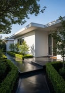 Charcoal lightly polished poured concrete covered entry porch, single-storey white render home with a flat roof,, clear blue-sky morning, even direct sun