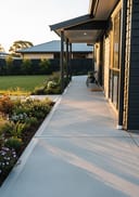 Light grey smooth raw pour poured concrete side-entry path, low-profile single-storey home with dark painted t, golden hour, warm low side light raking