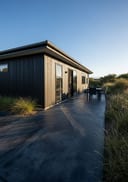 Near-black broom finish poured concrete patio, low-profile single-storey home with dark painted t, clear blue-sky morning, even direct sun