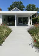 Light grey lightly polished poured concrete patio, single-storey white render home with a flat roof,, bright sunny midday, high sun, hard cris