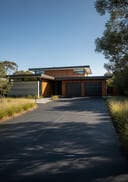 Charcoal smooth raw pour poured concrete driveway, single-storey flat-roof home with concrete-and-tim, mid-morning sun with soft tree-canopy sh