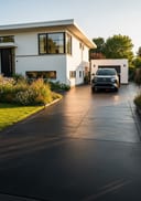 Near-black smooth raw pour poured concrete driveway, low-profile bungalow with white render walls, blac, golden hour, warm low side light raking